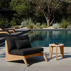 Outdoor lounge chair with black cushions and a small table by a pool
