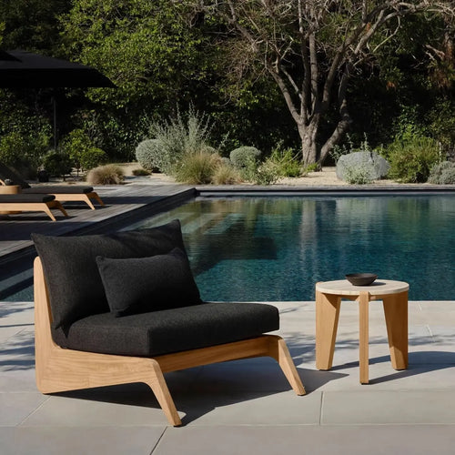 Outdoor lounge chair with black cushions and a small table by a pool