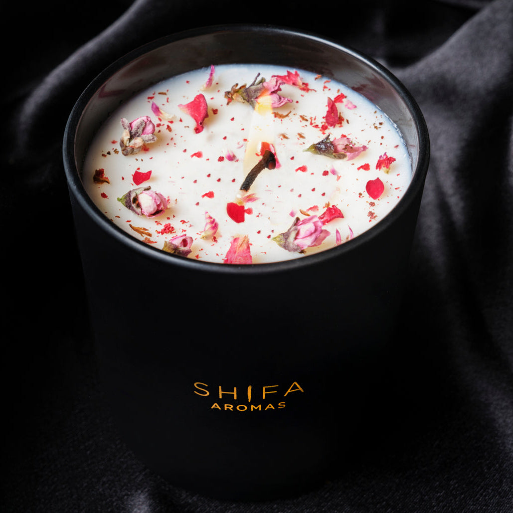 Black candle in a container with 'SHIFA AROMAS' branding on a dark fabric background