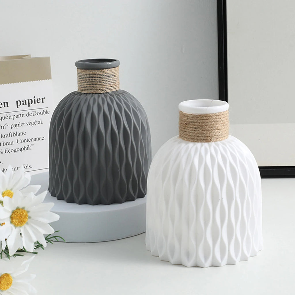 Two textured ceramic vases, one gray and one white, on a light surface with a neutral background.