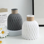 Two textured ceramic vases, one gray and one white, on a light surface with a neutral background.