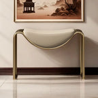 Modern console table with gold frame and white cushion against a wall with framed artwork.