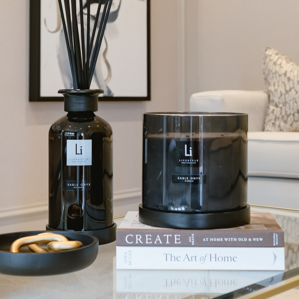Black candle and diffuser on books with a blurred living room background