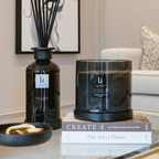 Black candle and diffuser on books with a blurred living room background