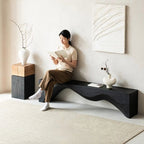 Woman sitting on a modern black bench reading a book in a minimalistic room.