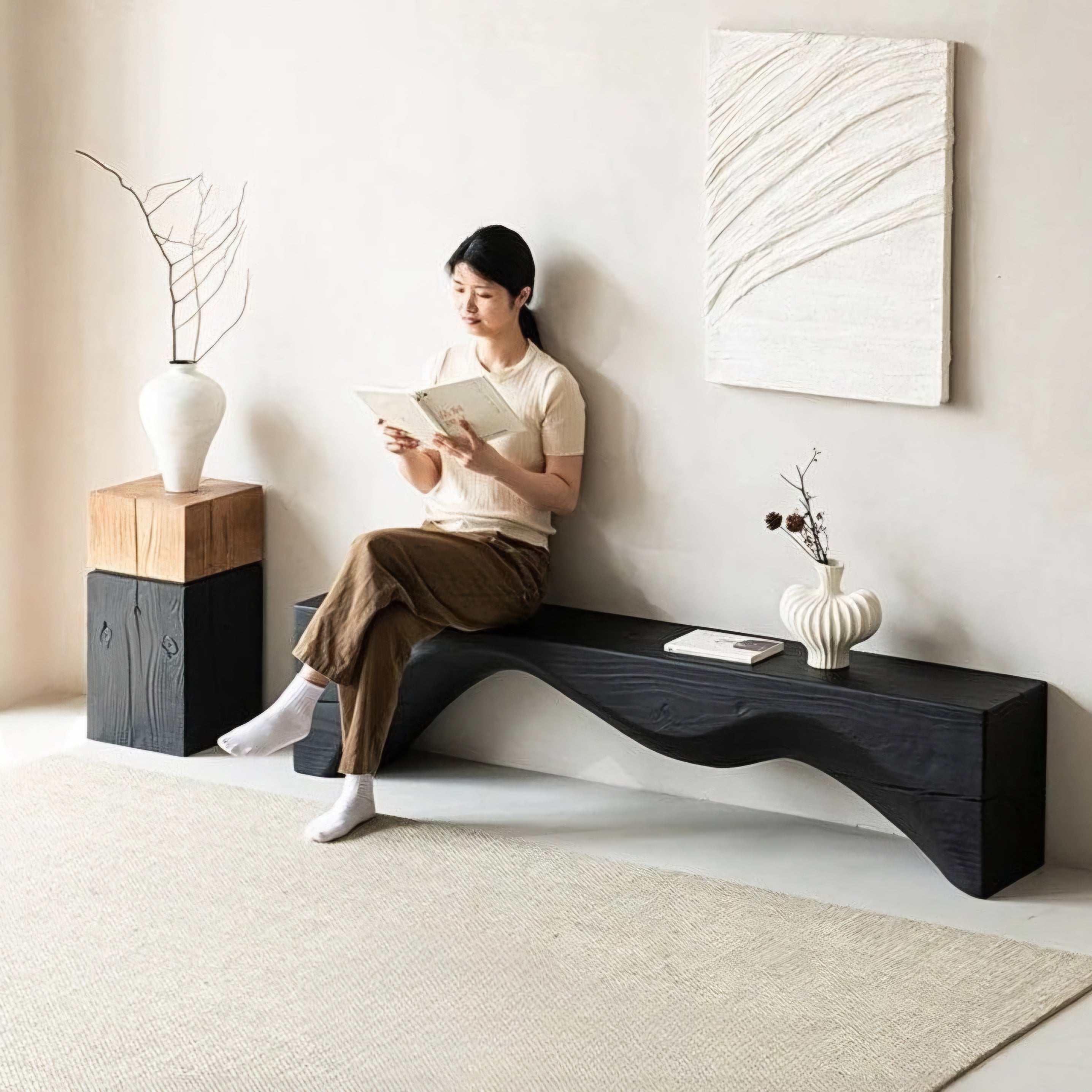 Woman sitting on a modern black bench reading a book in a minimalistic room.