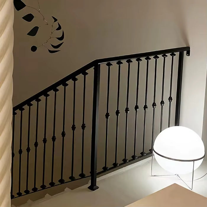 Black metal railing against a white wall with a modern floor lamp.