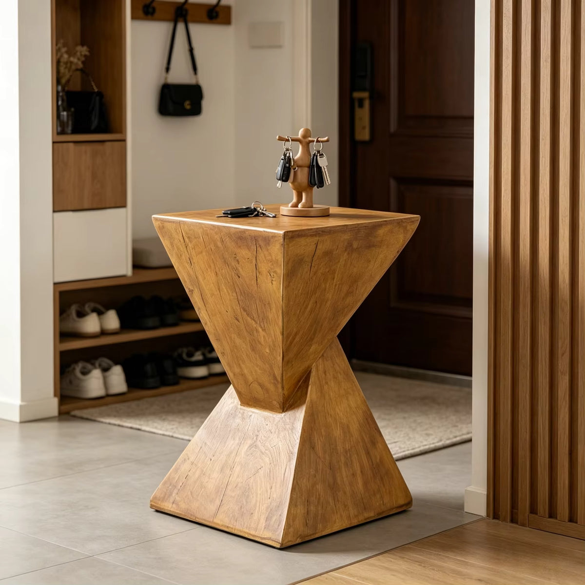 A geometric Concrete entryway table with a sculptural twisted base, styled in a modern home entryway with shoes on shelves, a door, and a small key holder on top.