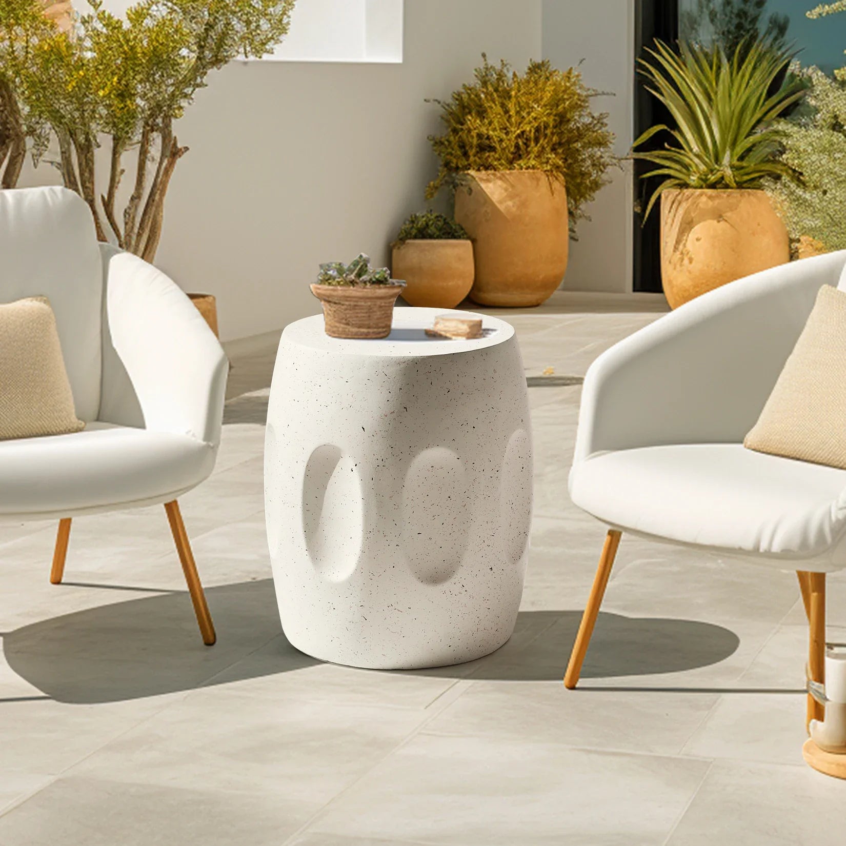 Outdoor patio setting with white chairs, a concrete side table, and potted plants.