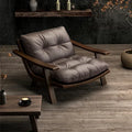 Gray cushioned chair with wooden frame in a dimly lit room with a coffee table and decorative items.