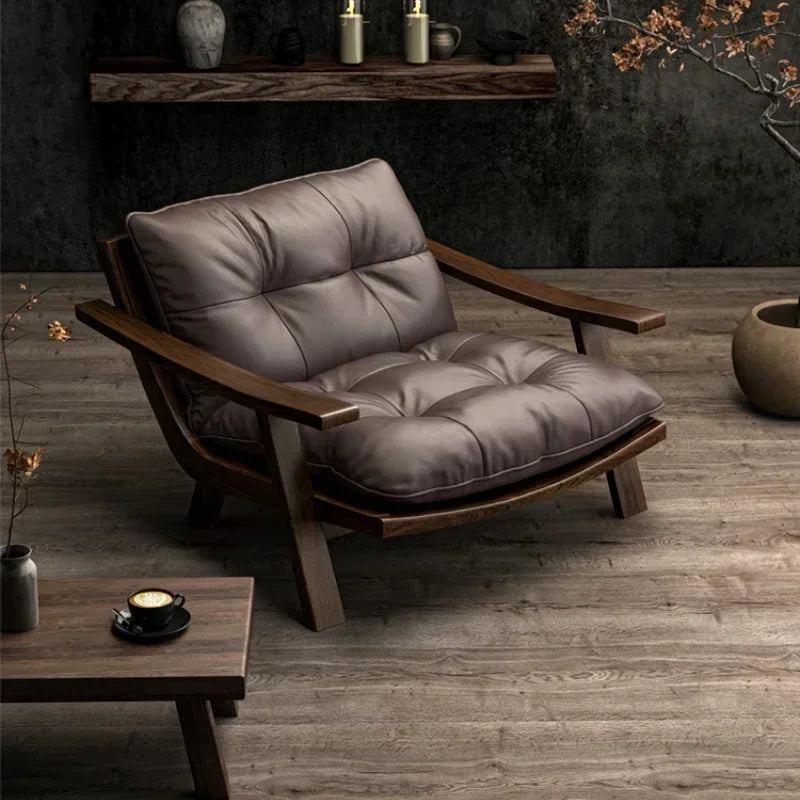 Gray cushioned chair with wooden frame in a dimly lit room with a coffee table and decorative items.