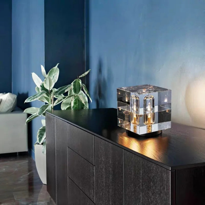 Modern interior with a black cabinet, clear crystal cube lamp, and green plant against a blue wall.