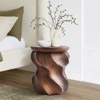 Wooden side table with wavy design holding a vase and branches in a living room setting.