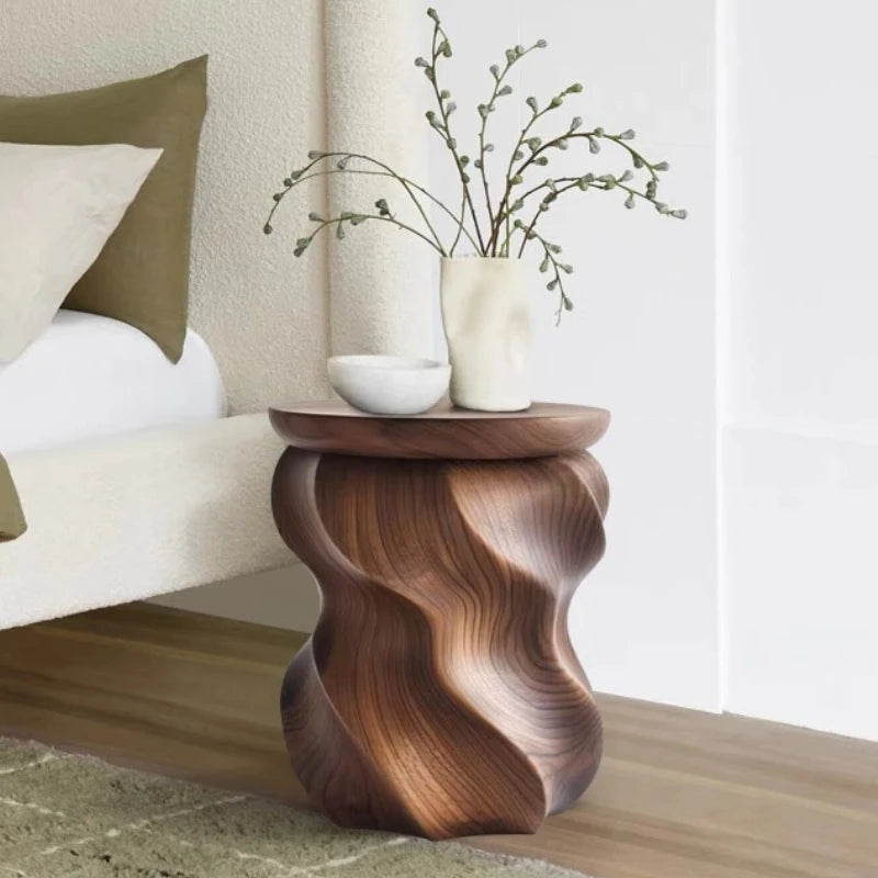 Wooden side table with wavy design holding a vase and branches in a living room setting.