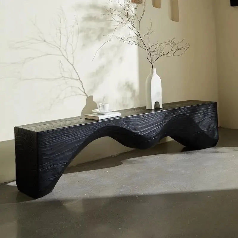 Modern black wavy coffee table with decorative items in a minimalistic room.