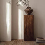 Decorative vase on a wooden pedestal against a neutral wall.