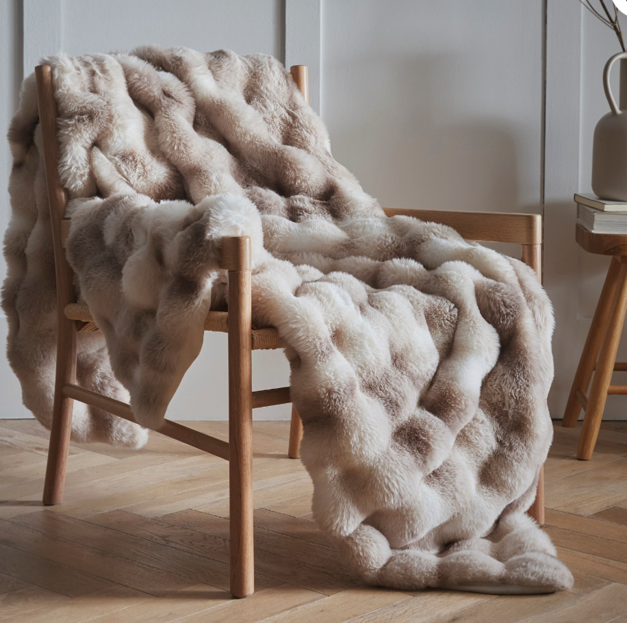 Beige fluffy blanket draped over a wooden chair in a room with a neutral color scheme.