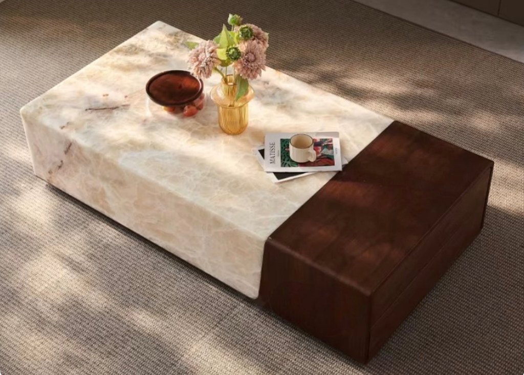 Marble coffee table with a brown upholstered end piece, featuring a cup, vase, and books on a gray carpet.