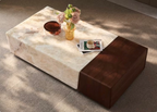 Marble coffee table with a brown upholstered end piece, featuring a cup, vase, and books on a gray carpet.