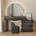Modern vanity setup with round mirror, desk, and chair in a well-lit room.
