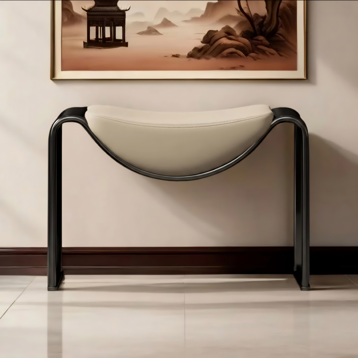 A modern console table with a curved cream-colored upholstered seat and a sleek black metal frame, positioned against a beige wall with a framed landscape painting above it.