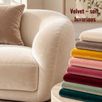 Luxury cream velvet sofa with rounded curves and matching cushion, beside a stack of colourful soft velvet fabric swatches in neutral, mustard, pink, burgundy, sage and teal tones.