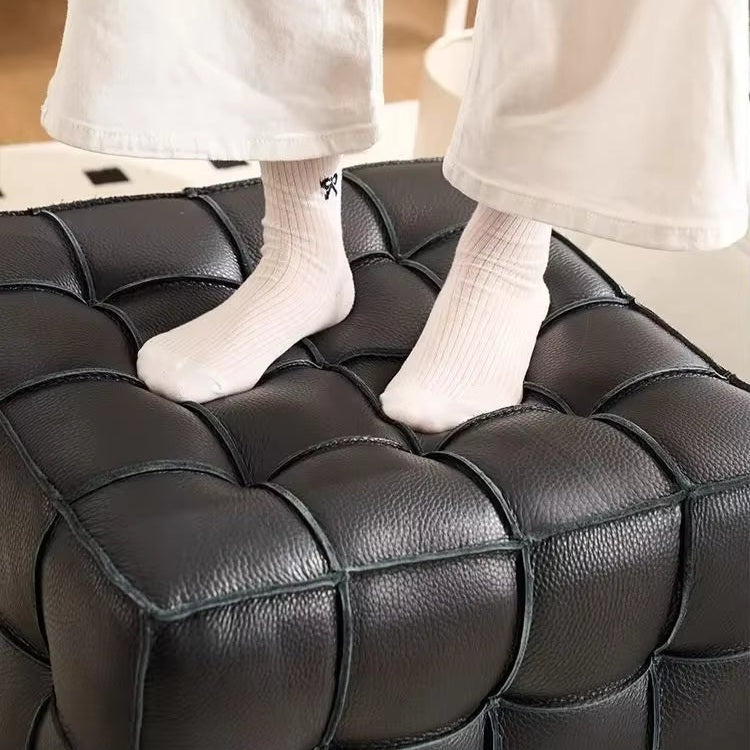 Person sitting on a black leather ottoman wearing white socks.
