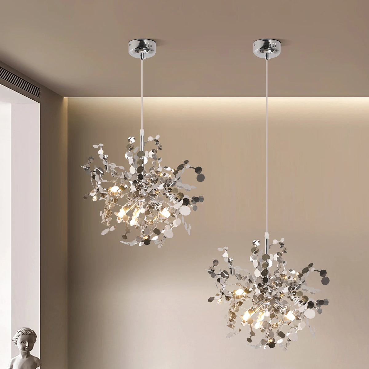 Two modern chandeliers hanging from the ceiling in a room with neutral walls.