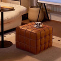 Brown leather ottoman in a living room setting with a coffee table and decorative items.