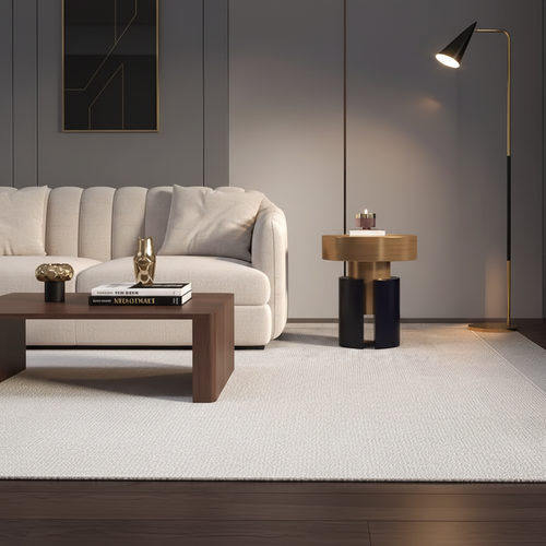A modern living room scene featuring a cream-colored sofa, a dark wood coffee table with books, a round gold and black side table, a black floor lamp, and a large white textured area rug on a dark wood floor.