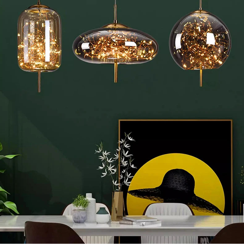 Three hanging glass pendant lights with decorative elements on a dark green wall.