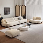 Modern living room with beige sofa, armchair, and ottoman on a wooden floor.