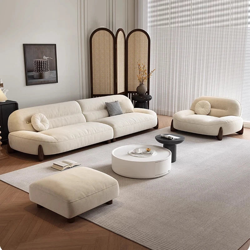 Modern living room with beige sofa, armchair, and ottoman on a wooden floor.