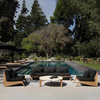 Outdoor patio set with black cushions by a pool surrounded by trees