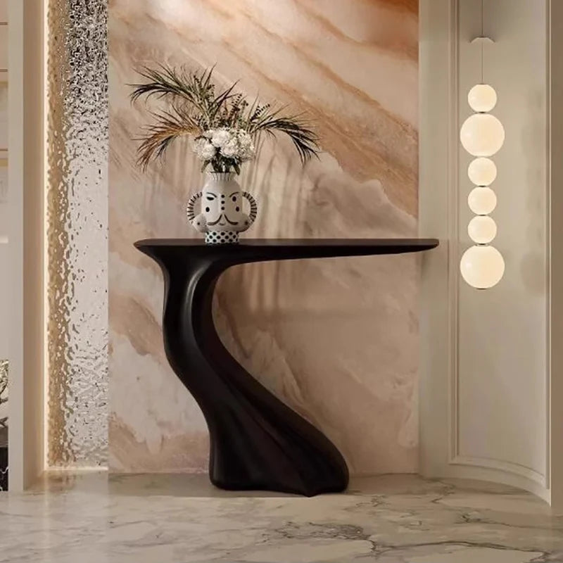 Modern black console table with decorative vase and flowers against a marble wall.