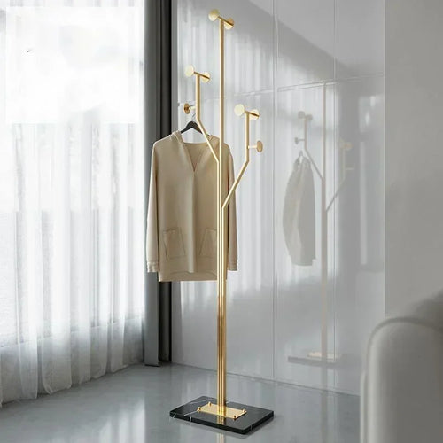 Gold coat stand with a beige coat against a white wall.