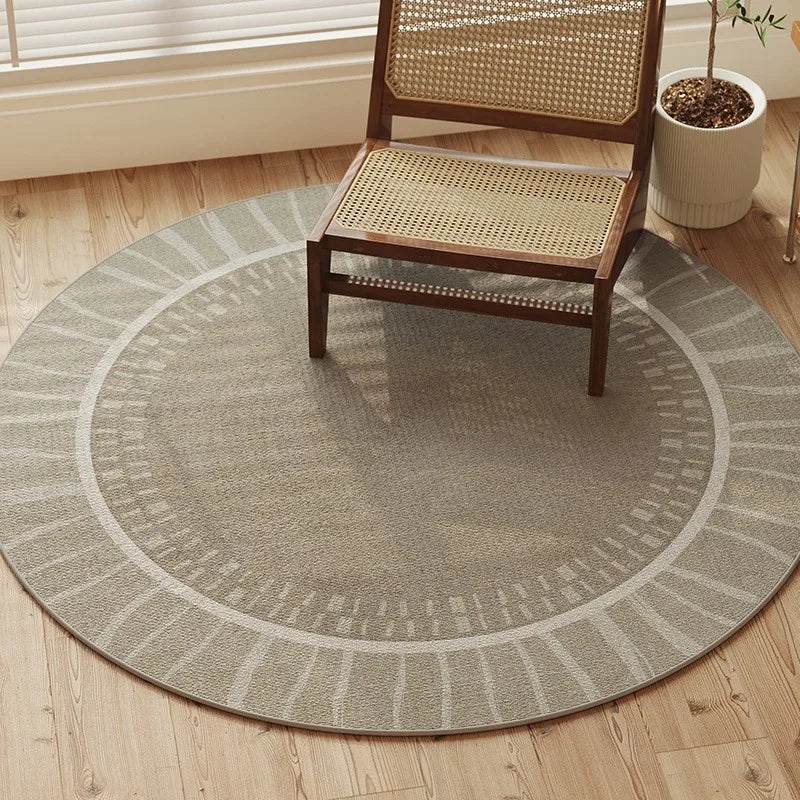 Round gray rug on a wooden floor with a wicker chair and plant in the background.