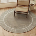 Round gray rug on a wooden floor with a wicker chair and plant in the background.