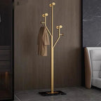 Gold coat rack with a beige coat against a brown wall.
