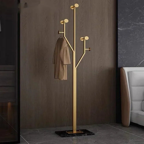 Gold coat rack with a beige coat against a brown wall.