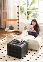Woman reading a magazine on a white sofa with a black leather cube ottoman in a modern living room.