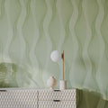 Decorative lamp and vase on a textured white console table against a green wavy patterned wall.