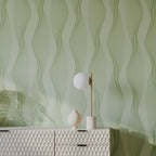 Decorative lamp and vase on a textured white console table against a green wavy patterned wall.