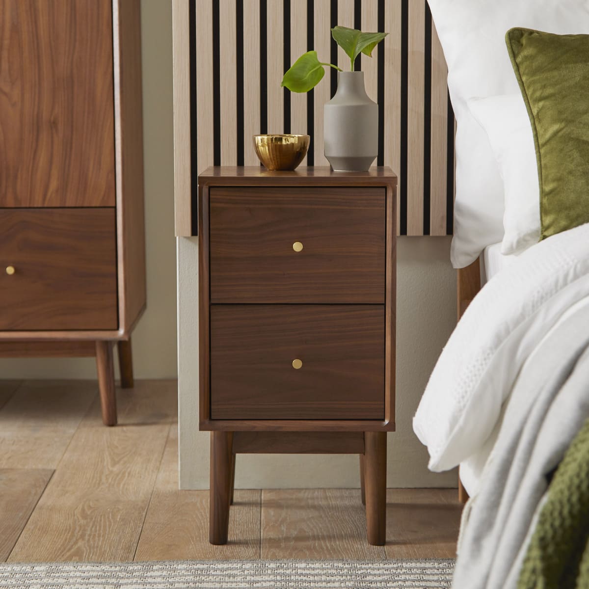 Wooden nightstand with two drawers next to a bed with green and white bedding.