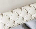 Close-up of a textured white headboard with pillows underneath.