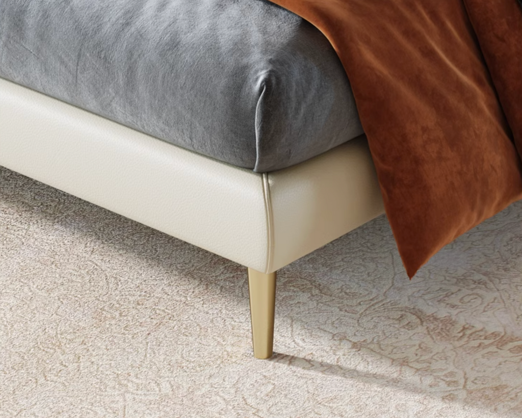 Close-up of a bed with gray mattress and brown blanket on a beige carpet.