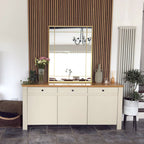 Beige sideboard with wooden top in a room with striped curtains and a mirror.