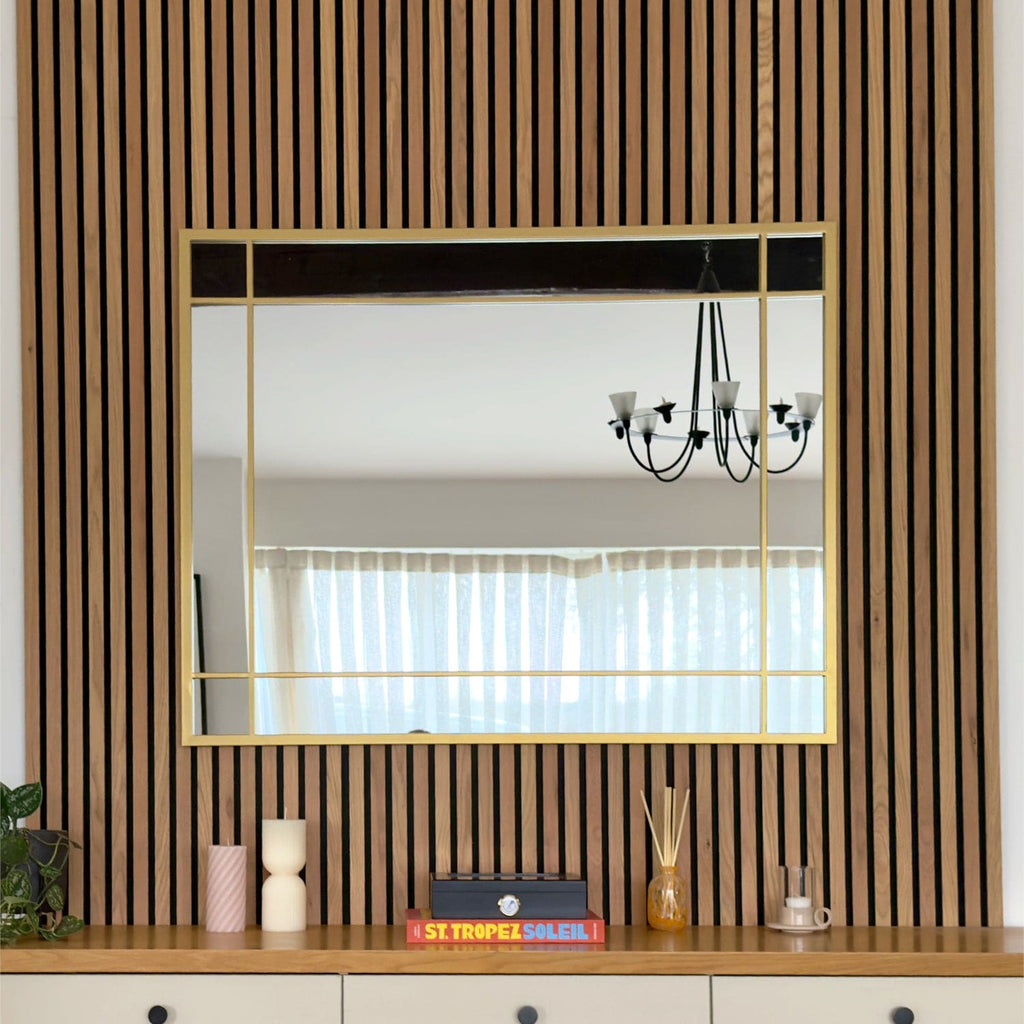 Wall mirror with gold frame on a wooden shelf against a striped wall.
