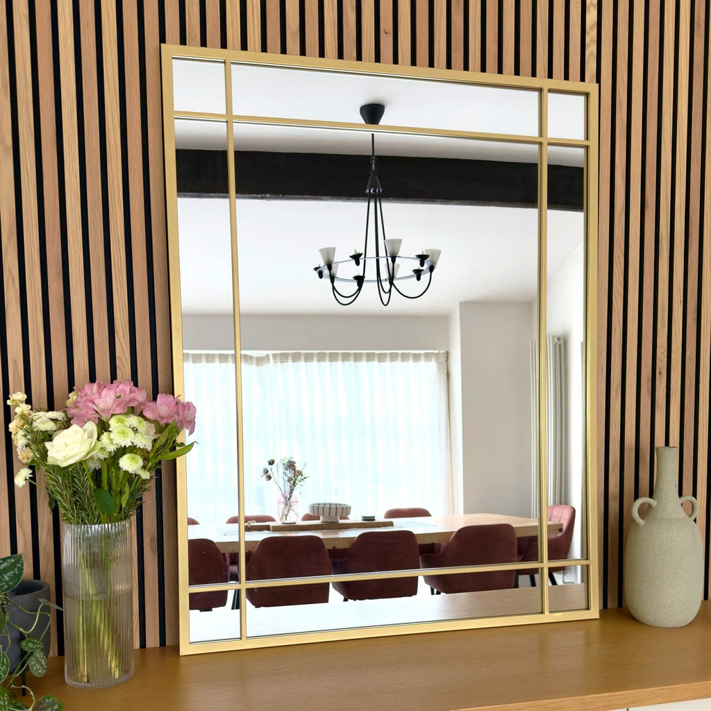 Large gold-framed mirror reflecting a dining room with a chandelier and table.