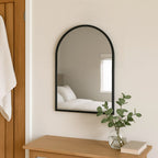 Arched mirror on a wall with a wooden side table and plant in the foreground